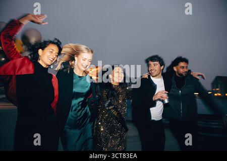 Fünf Freunde genießen sich abends im Freien, elegant gekleidet, lachen und verbinden sich, während sie gemeinsam feiern und eine fröhliche Atmosphäre schaffen Stockfoto