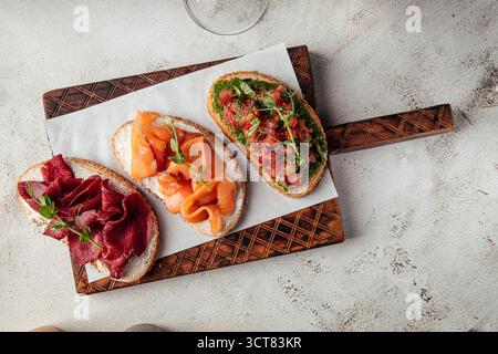 Drei offene Gourmet-Sandwiches auf Holzbrett Stockfoto