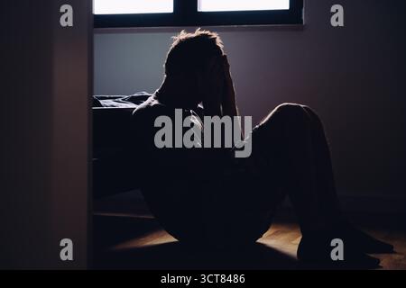 Silhouettenmann, der allein auf der Schlafzimmeretage sitzt, Symbol für Isolation, Depression und psychische Probleme. Selektiver Fokus. Stockfoto