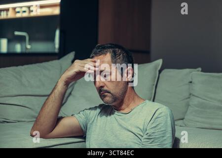 Schlafbedürftiger Mann in ungezwungener Wohnlage, in Einsamkeit zur Hand gebeugt, abendliche Innenstimmung. Selektiver Fokus. Stockfoto
