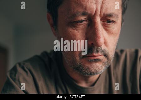 Porträt eines entmutigten erwachsenen Mannes, der mit traurigem Ausdruck nach unten blickt. Deprimierter Mann im Nahaufnahme-Porträt, Augen nach unten, Conce Stockfoto