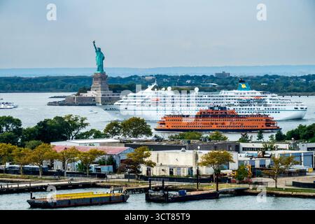 New York, NY - USA - 27. September 2025 Blick auf die Freiheitsstatue und ein Kreuzfahrtschiff im Hafen von New York, mit einer Staten Island Ferry, die am Gover vorbeigleitet Stockfoto