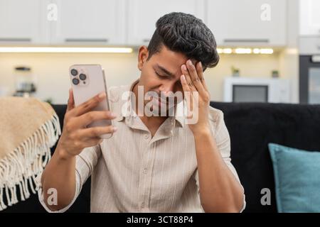 Der indische Mann zu Hause spielt die mobile Spielrunde verliert die Facepalm verärgert und ist bereit für das Rückspiel. Arabian Guy auf Sofa Tips versuchen Sie es erneut auf Smartphone Pläne Comeback konzentriert sich auf die nächste Stufe und die Wiederherstellung der Punktzahl Stockfoto