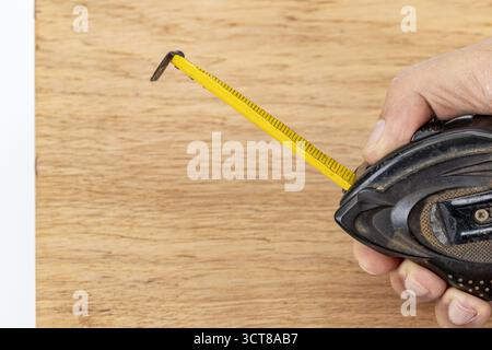 Ein Maßband gelbes Band Holzoberfläche Handwerkzeug Bau Schreinerei diy Werkstatt Präzisionsmessband erstreckt sich über Holz mit Handhaltung Stockfoto