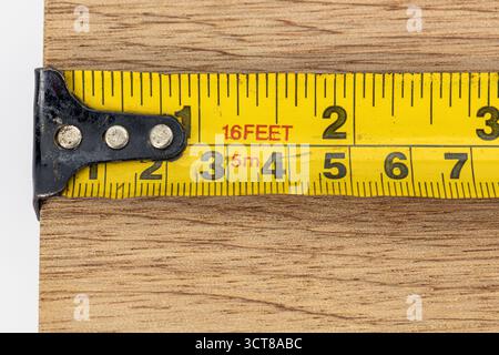 Ein gelbes Maßband mit Metallhaken Messskala metrische Zollholzdiele Nahaufnahme Werkstatttischerei heimwerker-Genauigkeitswerkzeug Stockfoto