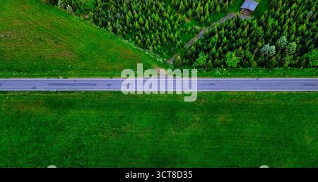 Luftaufnahme einer geraden Straße durch grüne Felder und Wälder, aufgenommen an einem hellen Sommertag. Stockfoto