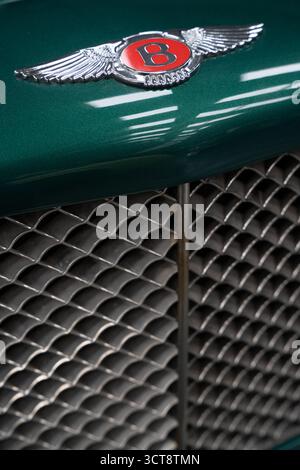 Nahaufnahme von Bentley geflügeltem Emblem und Chromgrill auf grünem Luxusauto Stockfoto
