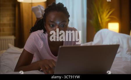 Afroamerikaner Familie verbringen Abend Internet Frau benutzen Laptop Ehemann Handy ethnisch verheiratetes glückliches Paar Bett zu Hause Schlafzimmer Nacht online Stockfoto