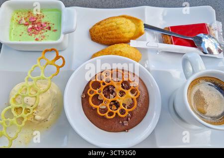 Moderne süße und elegante Dessertteller mit Schokoladenmousse, madeleine-Kuchen, Pistazien-Creme und Eis mit Zuckertuilgarnitur Stockfoto