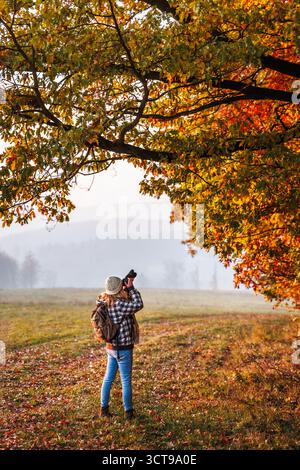 Frau mit Kamera, die bunte Herbstblätter in der Natur fotografiert. Wandern und Fotografieren Stockfoto