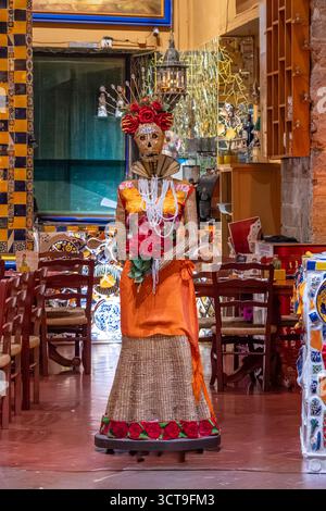 Eine Frau in einem Kostüm mit einer Blume in der Hand steht in einem Raum mit Stühlen und Tischen. Historisches Zentrum von Queretaro, Kolonialarchitektur, d Stockfoto