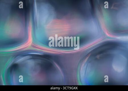 Abstrakte Nahaufnahme aus strukturiertem Glas mit abgerundeten Formen, die sanfte Blau-, Rosa-, Violett- und Grüntöne reflektieren und eine glatte schillernde wirkung erzeugen Stockfoto