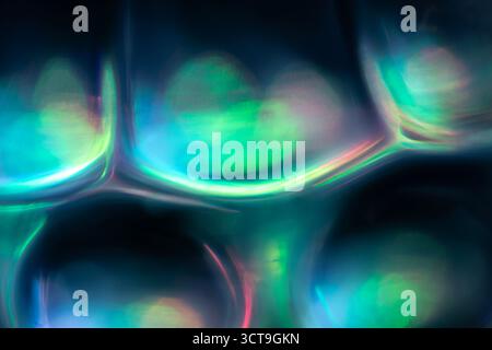 Abstrakte Nahaufnahme aus strukturiertem Glas mit abgerundeten Formen, die sanfte Blau-, Rosa-, Violett- und Grüntöne reflektieren und eine glatte schillernde wirkung erzeugen Stockfoto