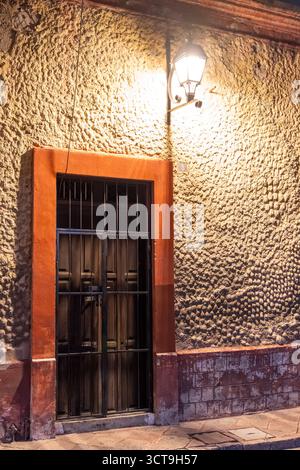 Ein dunkles Gebäude mit einer roten Tür und einem schwarzen Metalltor. Die Tür ist verriegelt und das Tor ist geschlossen. Historisches Zentrum von Queretaro, Kolonialarchitektur Stockfoto