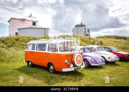 Alte Volkswagen-Käfer, darunter ein klassischer orangener Wohnmobil und zwei Käfer, die auf Gras in der Nähe alter Militärbunker am blyth Beach northumberland geparkt sind Stockfoto