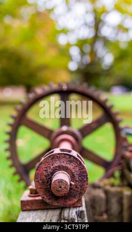 Nahaufnahme eines alten, rostigen Metallzahnrads und Achsmechanismus mit geringer Schärfentiefe in grüner Außenumgebung Stockfoto