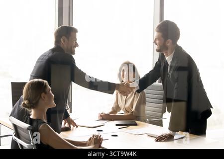 Zwei glückliche Millennial-Geschäftsmänner schütteln sich die Hände bei einem Rundtisch-Treffen Stockfoto