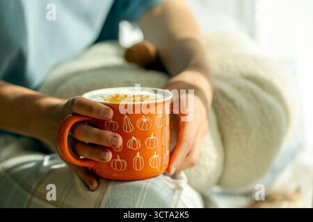 Person hält ein gemütliches Herbstgetränk in einem orangen Becher mit Kürbisillustrationen, Kürbislatte in niedlichem Becher mit Zimt, Herbststimmung Stockfoto