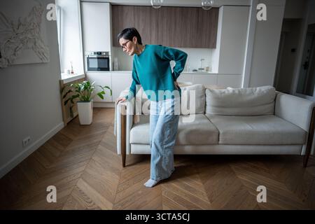 Frau, die sich unwohl rüberbummelte, versuchte zu stehen. Ischiasschmerzen, Bandscheibenvorfall, arthritische Probleme Stockfoto