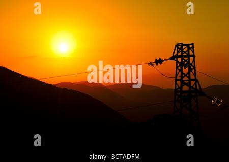 Goldener Sonnenuntergang mit Power Tower und Bergsilhouetten – Energie und Natur im visuellen Kontrast Stockfoto