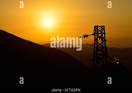 Goldener Sonnenuntergang mit Power Tower und Bergsilhouetten – Energie und Natur im visuellen Kontrast Stockfoto