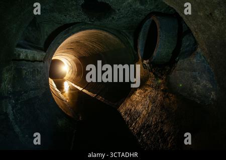 Innerhalb des unterirdischen städtischen Kanalisationssystems. Schmutziges Abwasser, das im runden Kanalrohr fließt. Stockfoto