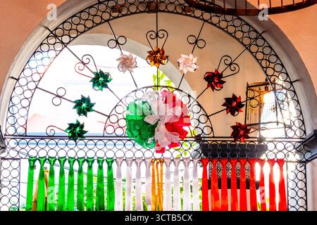 Ein farbenfroher Bogengang mit einem Kranz drauf. Der Kranz ist aus Papier und hat ein rot-weißes. Historisches Zentrum von Queretaro, Kolonialarchitektur, Dekor Stockfoto