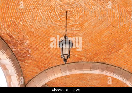 Eine Lampe hängt von der Decke in einem Raum mit einer roten Ziegeldecke. Die Lampe leuchtet auf. Historisches Zentrum von Queretaro, Kolonialarchitektur, Dekora Stockfoto