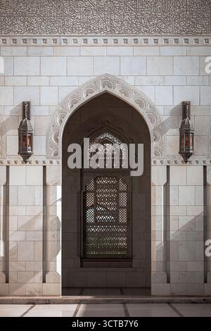 Wunderschöne islamische Architektur mit Bogengängen, geschnitzten Marmorwänden und einer hängenden traditionellen Laterne in der Sultan Qaboos Grand Moschee Stockfoto