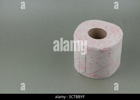 Dekorative Toilettenpapierrolle mit zartem rosa Design auf neutralem grauem Hintergrund verleiht der Badezimmereinrichtung einen Hauch von Charme und Kreation Stockfoto