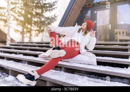Junge Frau genießt den Winter im Freien mit stilvollem Outfit auf Holztreppen in einer verschneiten Landschaft während Sonnenaufgang Stockfoto