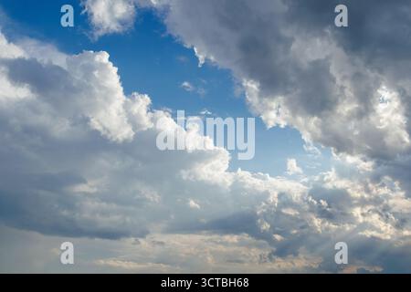 Eine malerische Aussicht auf einen hellblauen Himmel voller großer Kumuluswolken, beleuchtet von sanftem Sonnenlicht, das durch die Luft strömt, und schafft eine dramatische und friedliche Atmosphäre Stockfoto