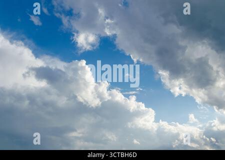 Eine malerische Aussicht auf einen hellblauen Himmel voller großer Kumuluswolken, beleuchtet von sanftem Sonnenlicht, das durch die Luft strömt, und schafft eine dramatische und friedliche Atmosphäre Stockfoto