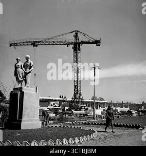 Der Bau des Puschkin Boulevard (heute Schewtschenko Boulevard) in Sloviansk, ukrainische SSR, in den 1960er Jahren Diese Fotos zeigen die Schaffung eines neuen öffentlichen Raumes mit Statuen des sozialistischen Realismus, die auf einer aktiven Baustelle installiert sind. In neu geformten Blumenbeeten stehen Denkmäler, die die idealisierte sowjetische Jugend und Mutterschaft darstellen, während im Hintergrund ein großer Turmkran arbeitet. Diese Gegenüberstellung von fertiger Kunst und roher Konstruktion war typisch für diese Zeit und symbolisierte die ideologischen Grundlagen, die für die neue Stadt gelegt wurden Stockfoto