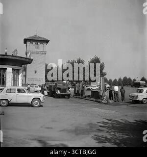Eine belebte Tankstelle (AZS) in Sloviansk, ukrainische SSR, Ende der 1950er Jahre Dieses Archivfoto zeigt eine typische Szene aus der frühen Ära der sowjetischen Automobilisierung. Ein klassischer GAZ-M20 Pobeda und ein neuerer Moskvitch-407, legendäre Autos dieser Zeit, werden beim Tanken gesehen. Die Vintage-Pumps im Säulenstil und das Warnschild „Rauchen ist gefährlich!“ Tragen Sie zur authentischen Atmosphäre bei. Dieses Bild eines Schlüsselstücks der städtischen Infrastruktur ist ein mächtiges Symbol für die Modernisierung der Stadt nach dem Krieg und die zunehmende Mobilität ihrer Bevölkerung Stockfoto