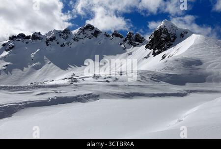 Skifahrer stehen auf einem verschneiten Berghang mit malerischem Schnee - bedeckte Gipfel im Hintergrund unter einem blauen Himmel mit Wolken. Österreich - Obertauern Stockfoto