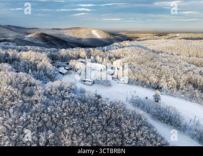 Aus der Vogelperspektive auf den Schnee, die Straße, den Wald im Winter. Blick von der Drohne auf das Bergdorf, schneebedeckte Kiefern bei Sonnenaufgang in der Slowakei Stockfoto