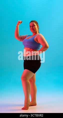 Kurvige Fitness-Frau biegt den Arm in Sportbekleidung mit freudiger Energie Stockfoto