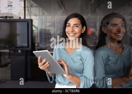 Glückliche junge lateinische Geschäftsfrau, die ein Tablet hält Stockfoto