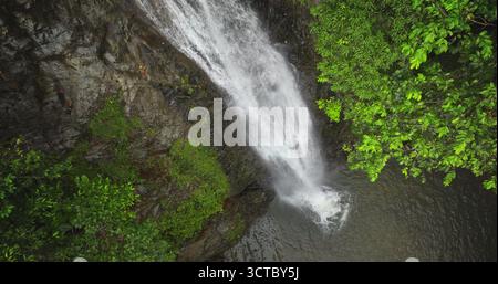 Fidschi, Nadi Wasserfall: Nahaufnahme atemberaubender Wasserfall, der eine felsige Klippe hinunterstürzt, lebendige grüne Baldachin aus üppigem Regenwald. Atemberaubender Blick aus der Vogelperspektive zeigt die wilde Naturlandschaft. Drohnenflug Stockfoto