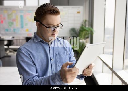 Ernsthafter Geschäftsmann mit Down-Syndrom, der mit Tablette arbeitet Stockfoto