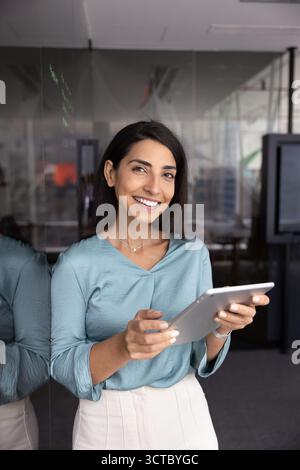 Glückliche hispanische Geschäftsführerin, die an der Glasplatte des Büros steht Stockfoto