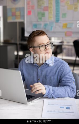 Nachdenklicher männlicher Angestellter mit Down-Syndrom, der über Geschäftsprojekte denkt Stockfoto