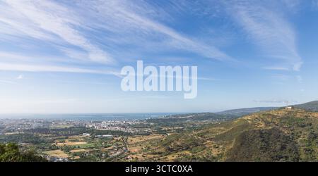 Weitläufiger Blick auf die Landschaft von den Hügeln von Arrabida, zeigt die Stadt Setubal in der Ferne und das Meer und die Halbinsel Tróia unter einem weiten Himmel. Stockfoto