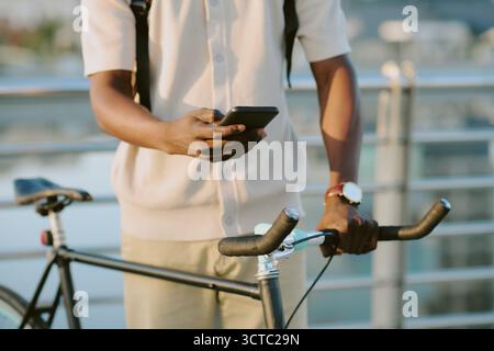 Junger Erwachsener Schwarzer Mann, Der Das Smartphone Benutzt, Während Er Draußen Neben Dem Fahrrad Steht Stockfoto
