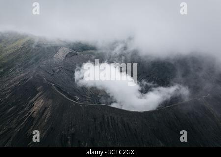 Aus der Vogelperspektive des Vulkankraters Bromo, wo Wolkenfetzen mit dem dunklen vulkanischen Felsen tanzen und einen ätherischen Tanz aus Licht und Schatten erzeugen, Mt. B Stockfoto