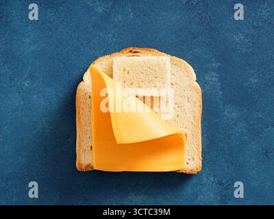 Kreatives Stillleben von einem Stück Brot und Käse, das einem Bett ähnelt. Minimale konzeptionelle Lebensmittelkunst auf blauem Hintergrund. Essen vor dem Schlafengehen. Stockfoto