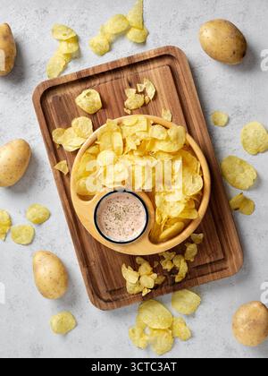Knusprige Kartoffelchips und eine geschmackvolle Dippsauce serviert auf einer Holzplatte, perfekt für Partyjause oder Junk Food-Genuss Stockfoto