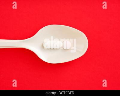 Weißer Löffel mit Medikamententabletten und Tabletten auf einem leuchtend roten Hintergrund, der Gesundheits- und Wellnesskonzepte veranschaulicht. Tagesdosis. Stockfoto