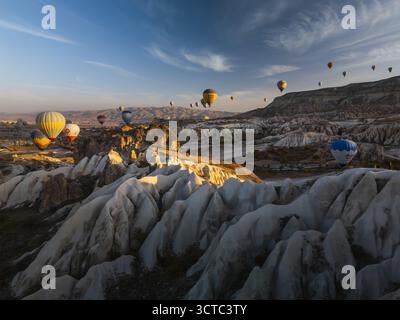 Aus der Vogelperspektive sehen Sie lebendige Heißluftballons, die über die surrealen, skulpturalen Landschaften Kappadokiens treiben, die in Morgentönen gemalt sind, Goreme, Nevsehir und Turkiye. Stockfoto
